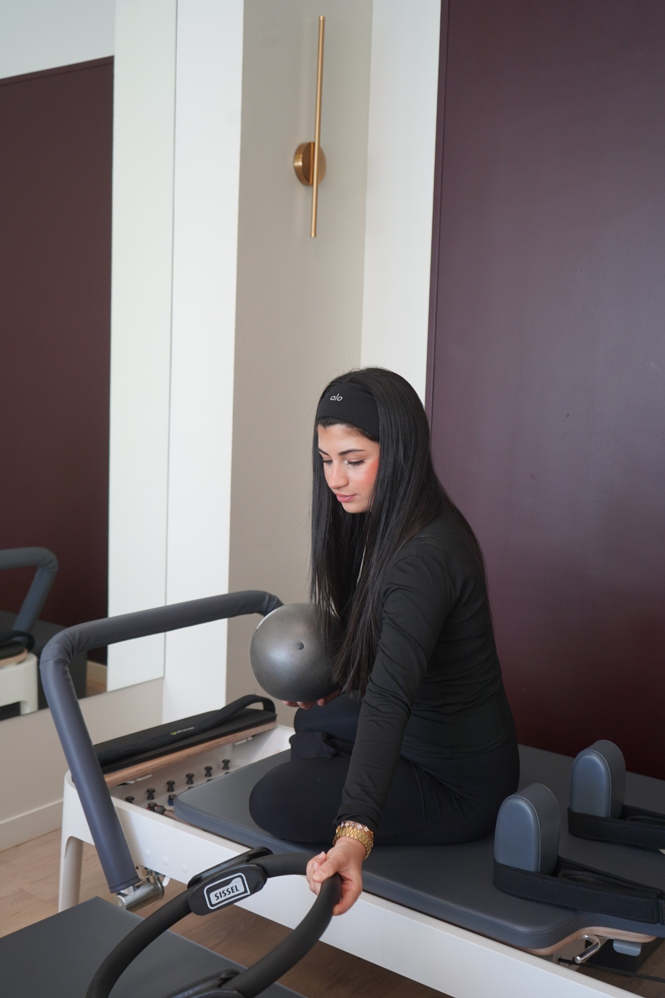 Instructor seated on a Pilates reformer holding a weighted ball at Hype Studio