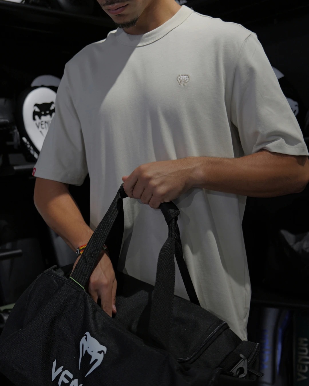 Man holding a black Venum duffel bag, wearing a beige t-shirt