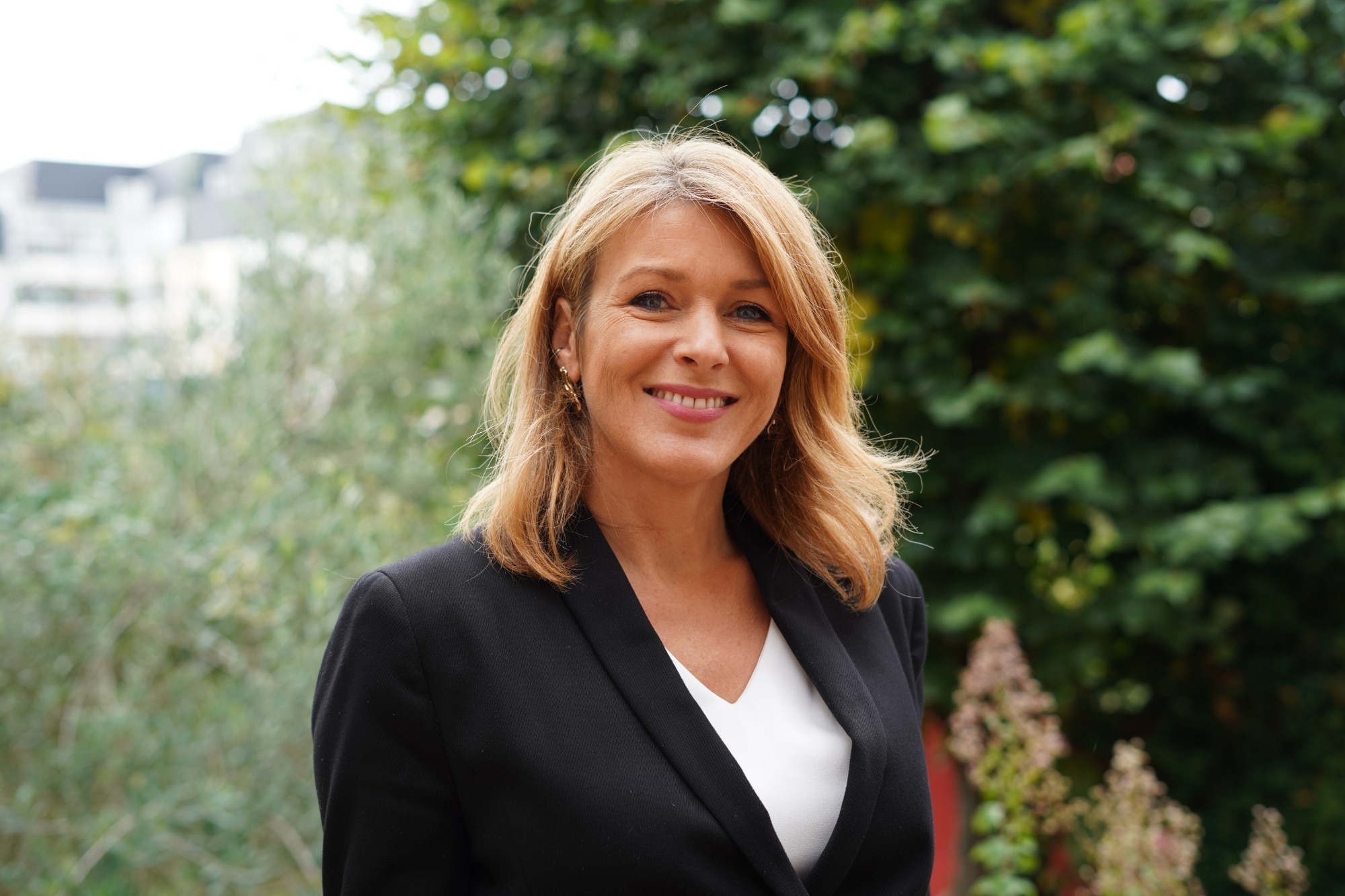 Portrait of a blonde woman in a black blazer smiling outdoors